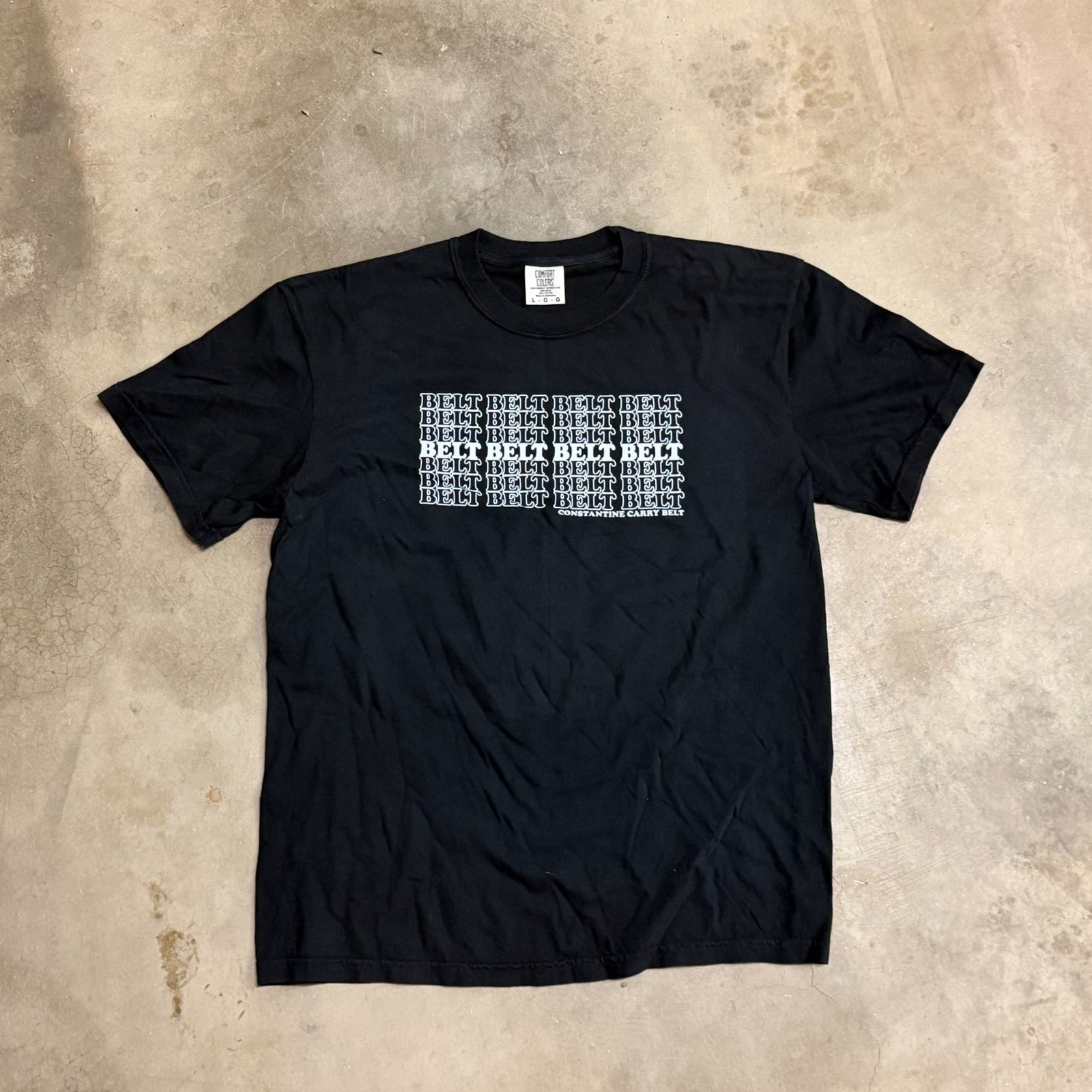 Black t-shirt with white text on a beige concrete surface