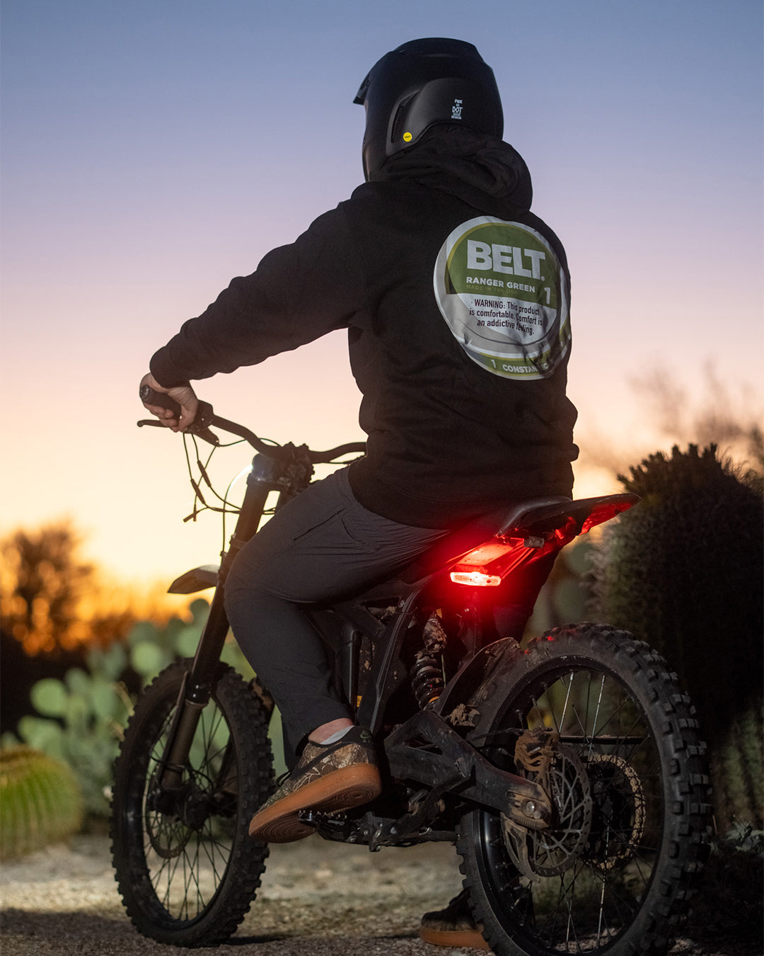 Rider on an electric dirt bike at sunset, wearing the Zyn Belt Hood