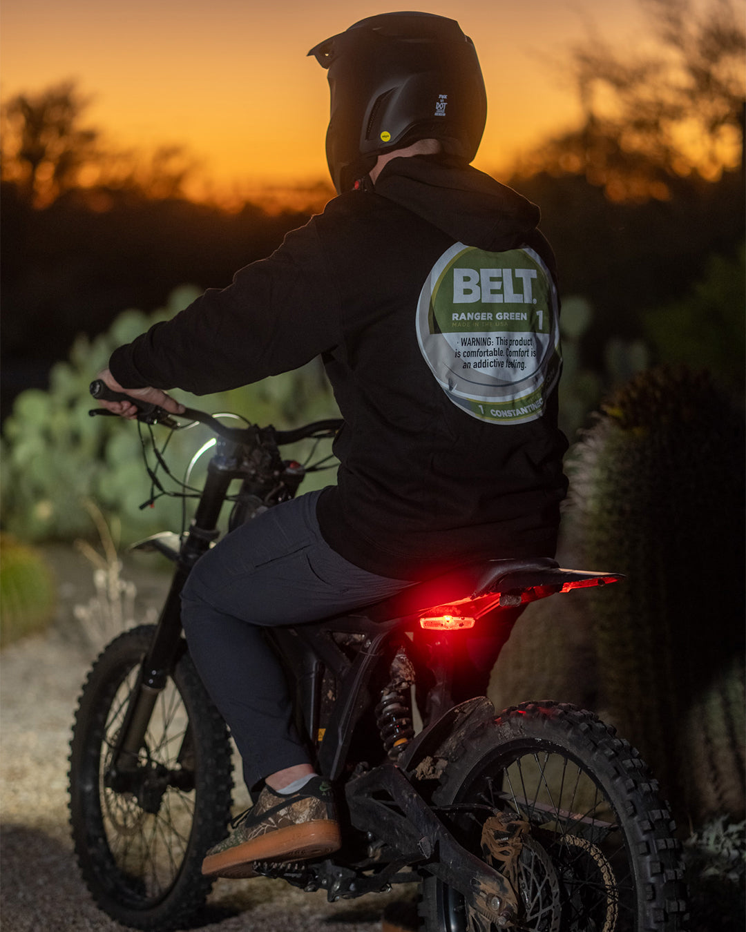 Rider on an electric dirt bike at dusk, back graphic of the Zyn Belt Hood showing