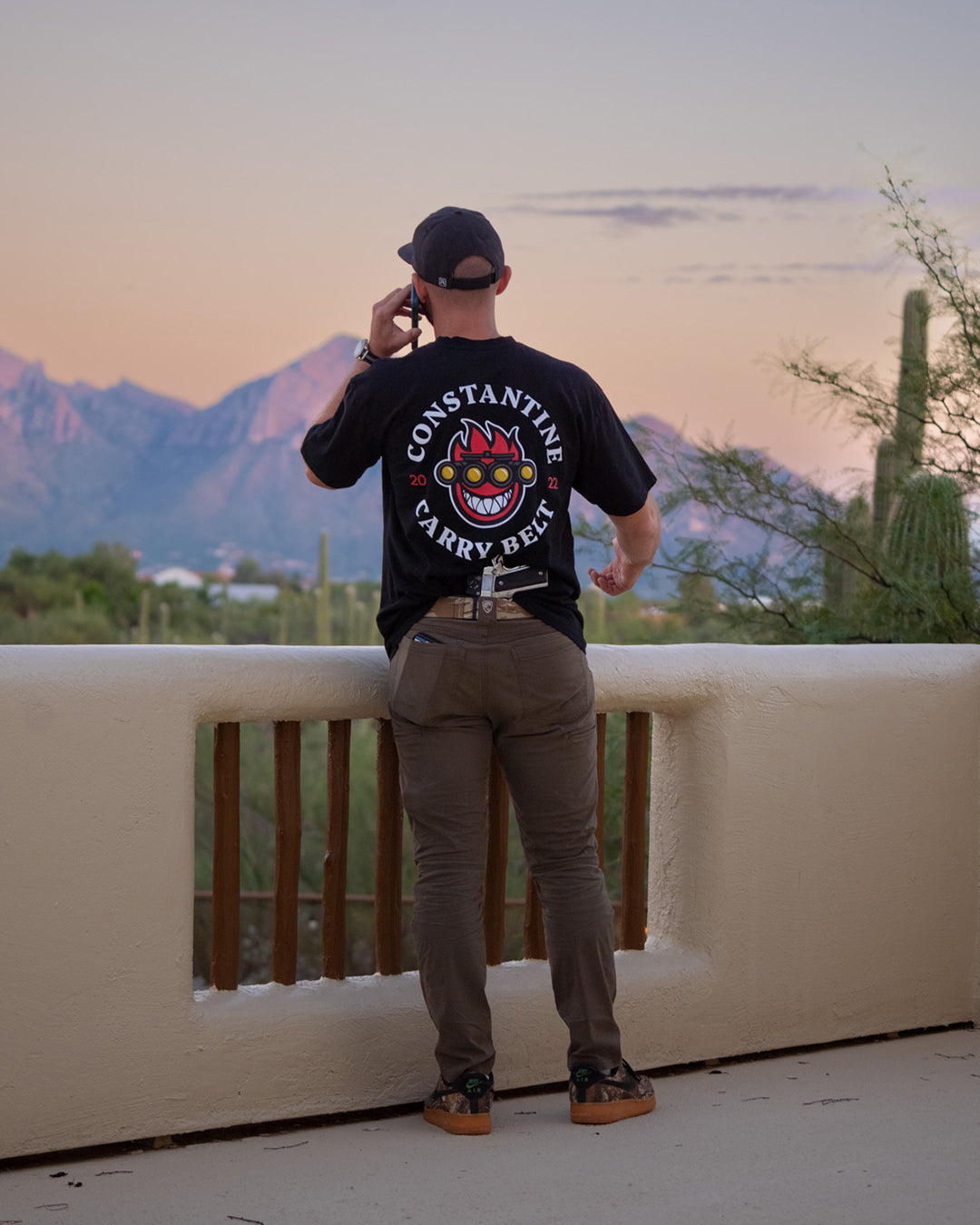 Man on a balcony overlooking the mountains in the Spitfire Belt Tee, back view