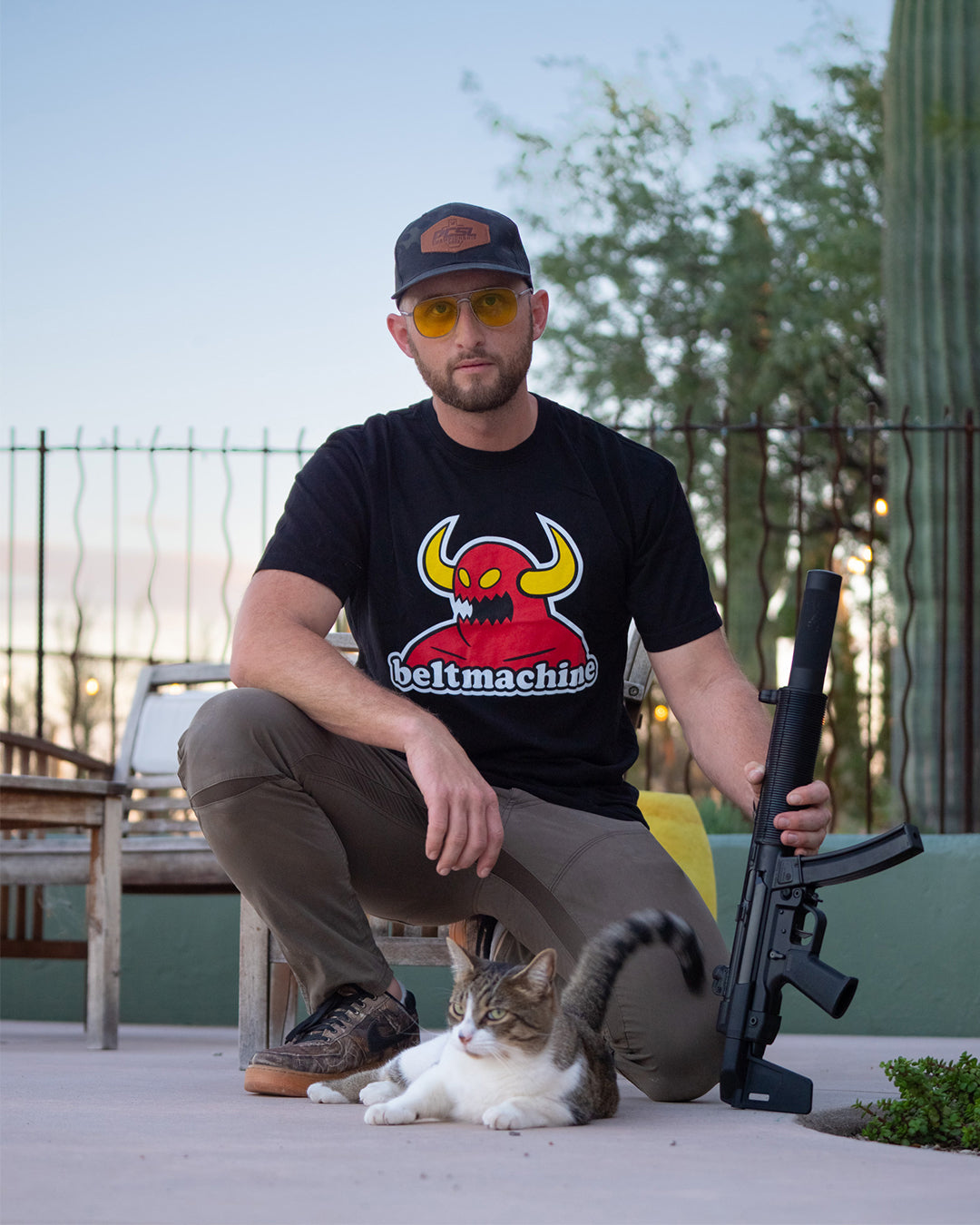 Man kneeling outdoors next to a cat in the Belt Machine Tee