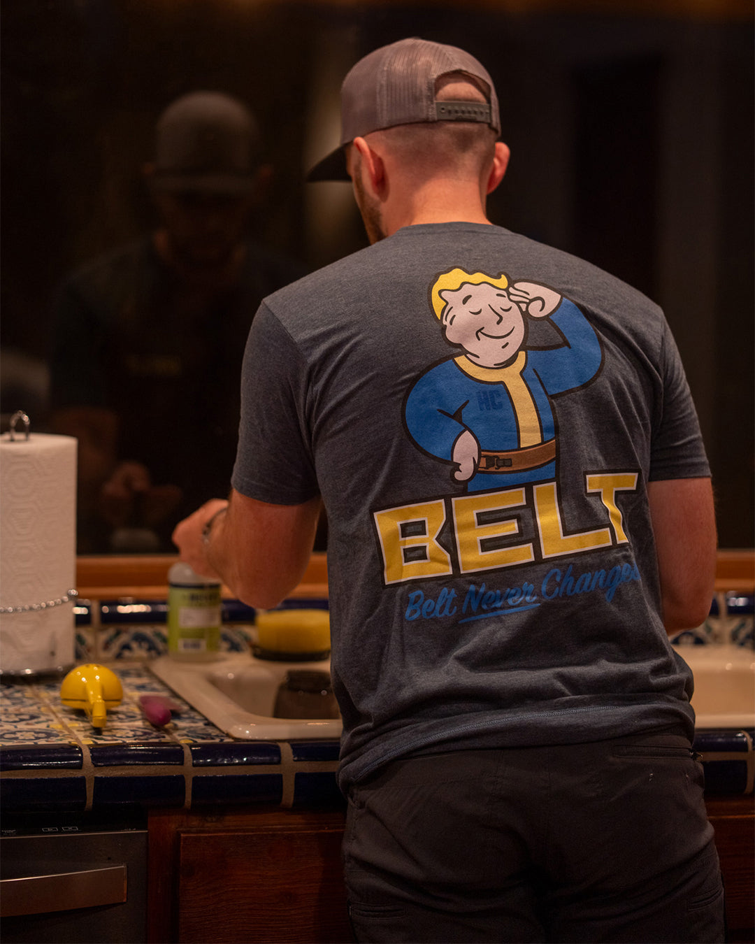 Man in a kitchen wearing the Fallout Belt Tee, graphic on his back