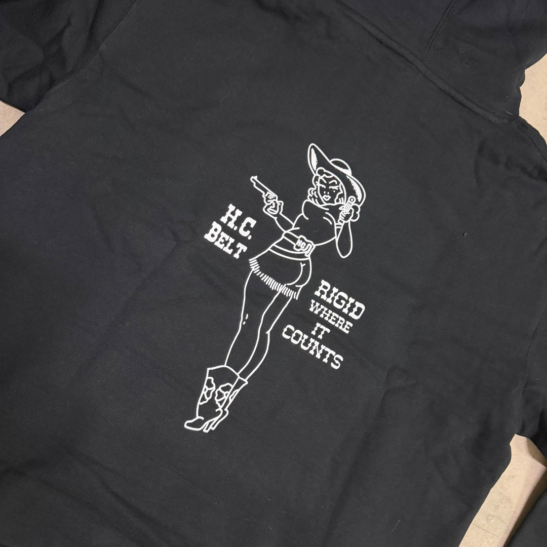 Black t-shirt with white graphic design of a woman in a cowboy outfit and text on a beige surface.