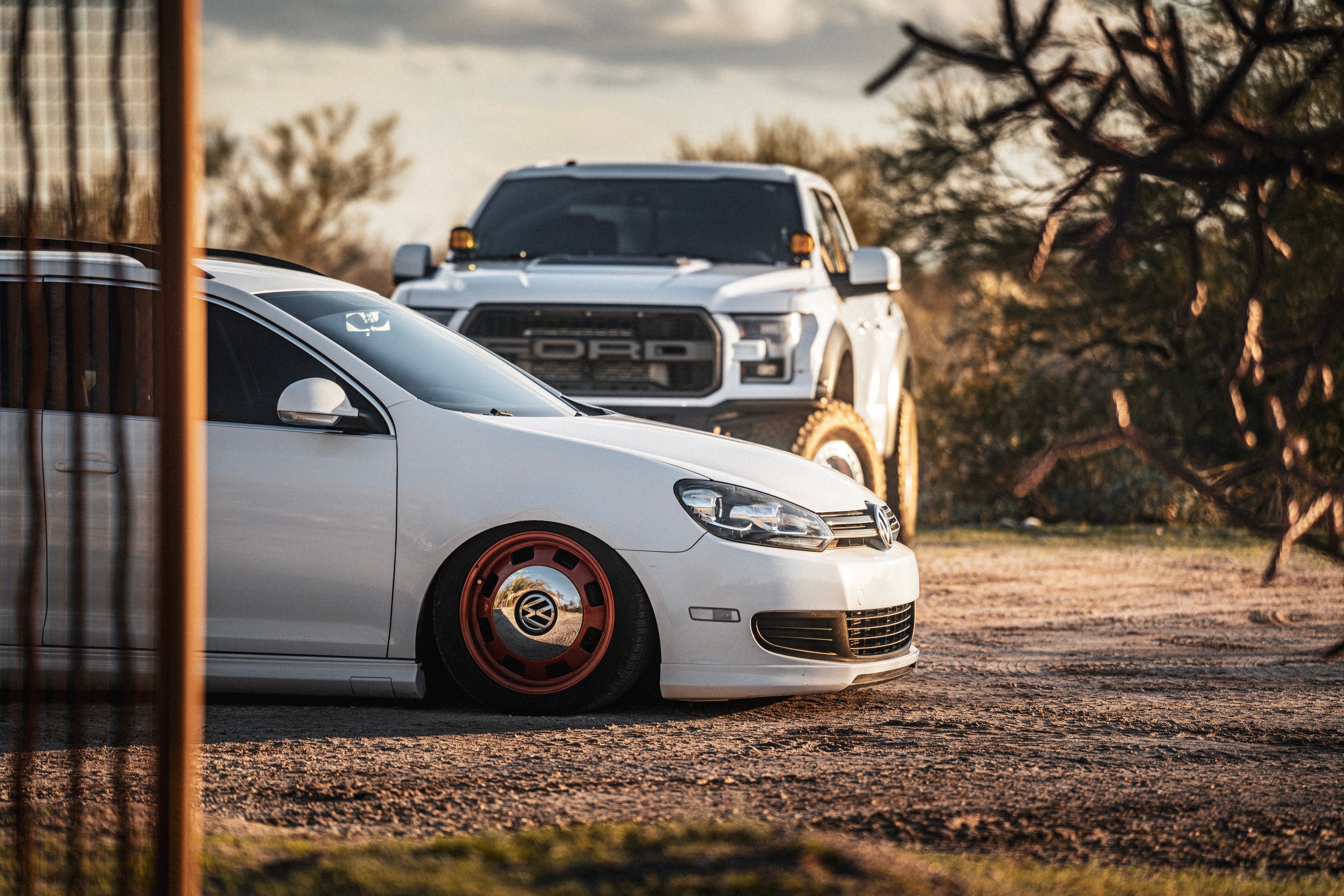 Two cars, one white and one with a visible Ford logo, on a dirt road with desert landscape.
