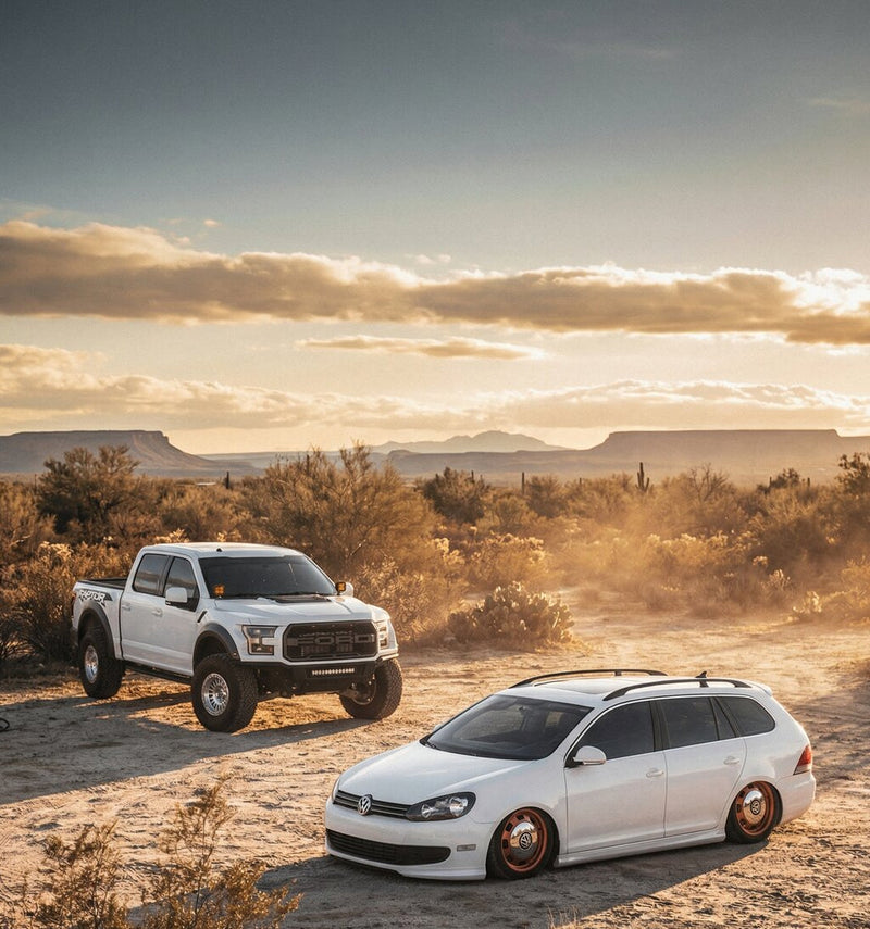 Two white vehicles parked in a desert landscape with a sunset sky.