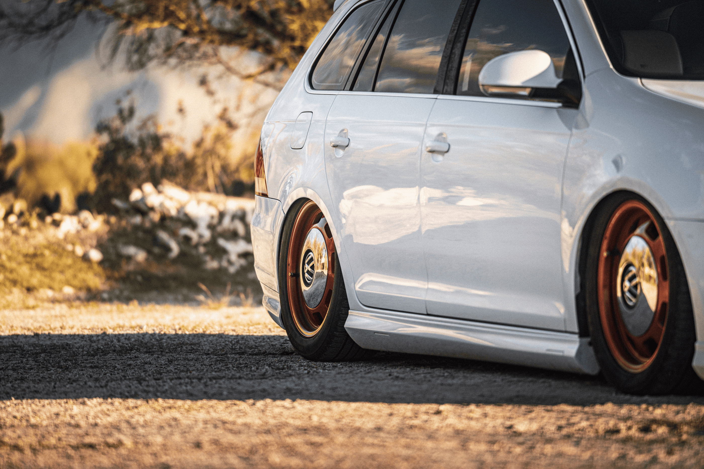 White car with orange rims parked on a dirt road with a blurred natural background
